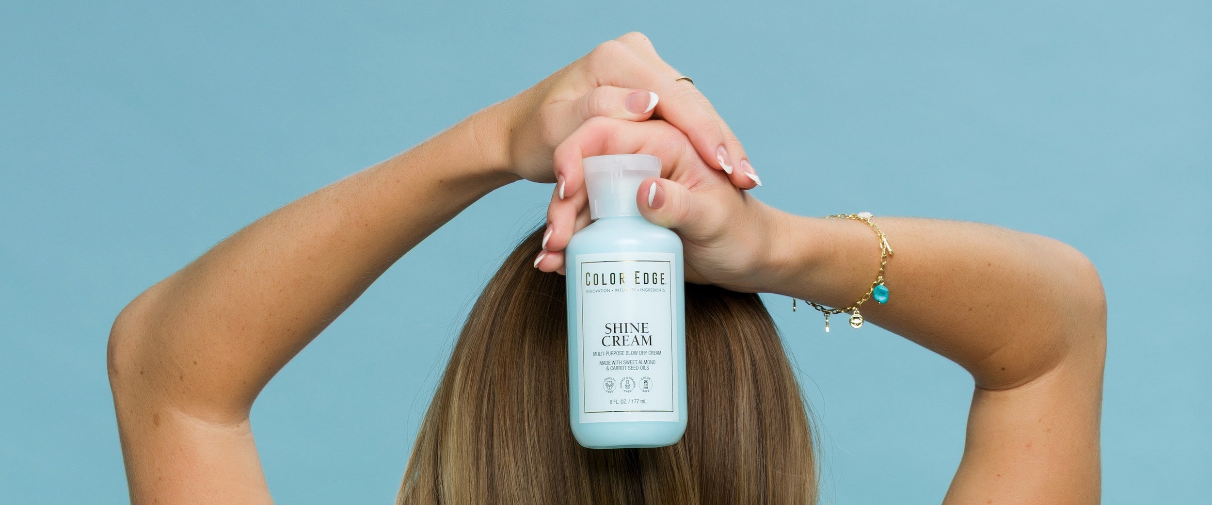 Woman holding bottle of Shine Cream against a blue background