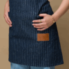 Blue denim pinstriped apron. Closeup details of the leather logo patch